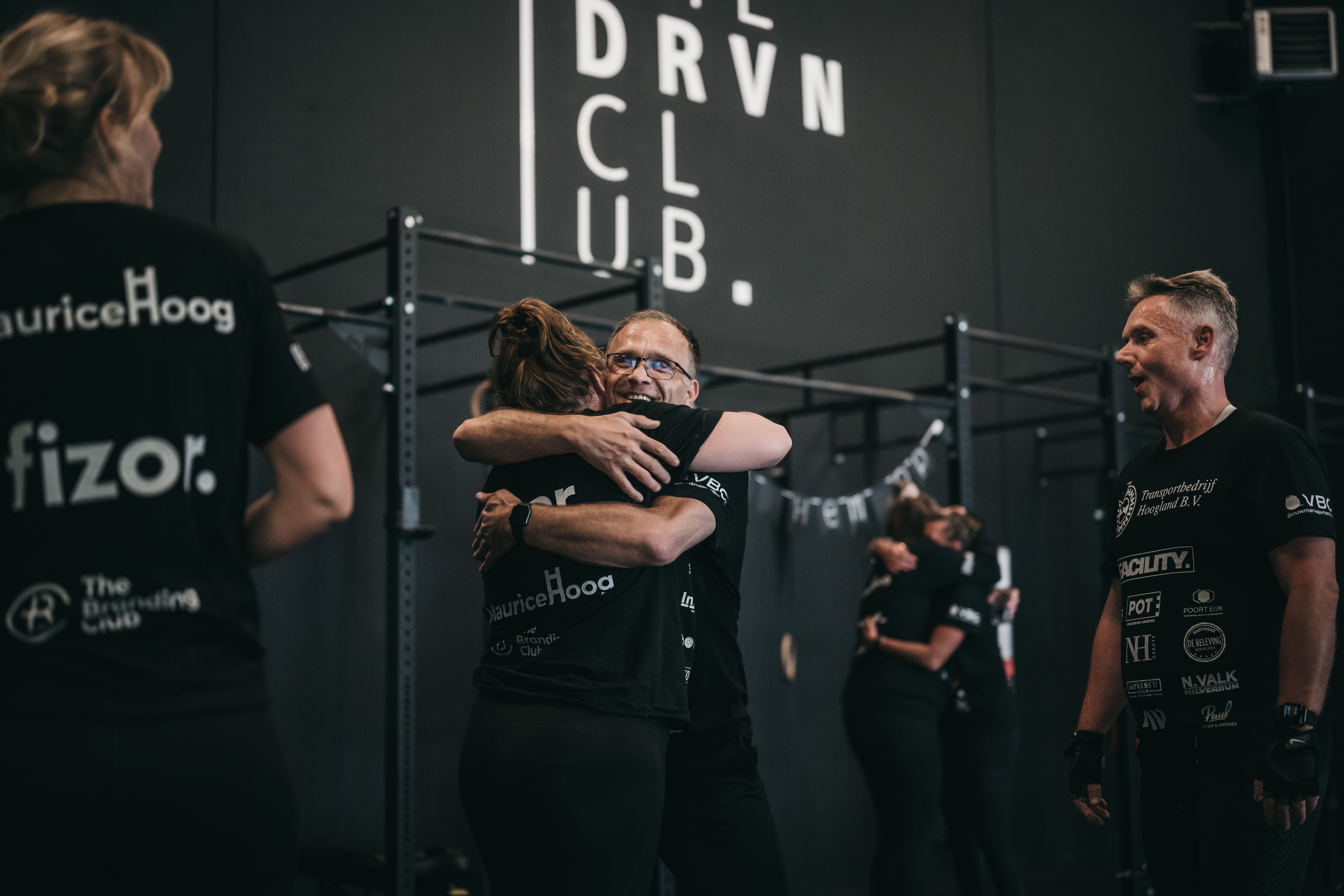 Mensen begroeten elkaar in de trainingsruimte van The Driven Club, met het clublogo op de muur